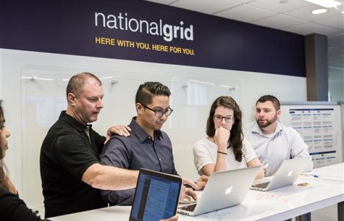 Five National Grid representatives working at a high desk with a white board in the background 